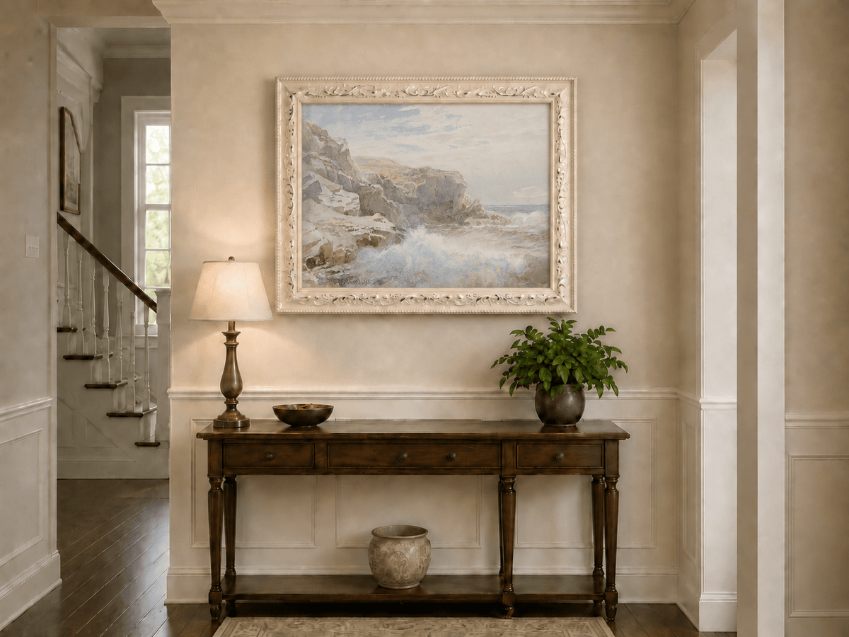 Framed hand-painted coastal cliffs oil painting with waves crashing against pale rocks displayed above an entryway console table.