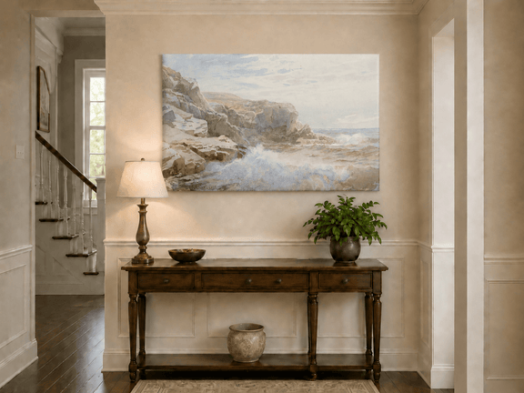Unframed hand-painted coastal cliffs oil painting with waves crashing against pale rocks displayed above an entryway console table.