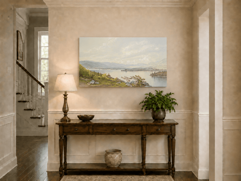 Unframed hand-painted expansive lake oil painting with distant mountains, trees and calm water displayed above an entryway console table.