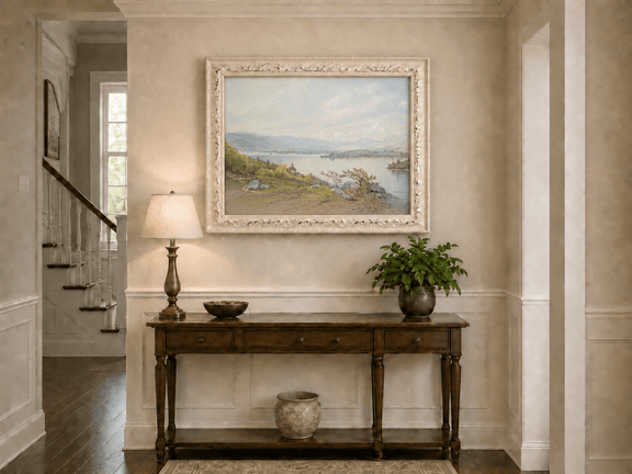 Framed hand-painted expansive lake oil painting with distant mountains, trees and calm water displayed above an entryway console table.
