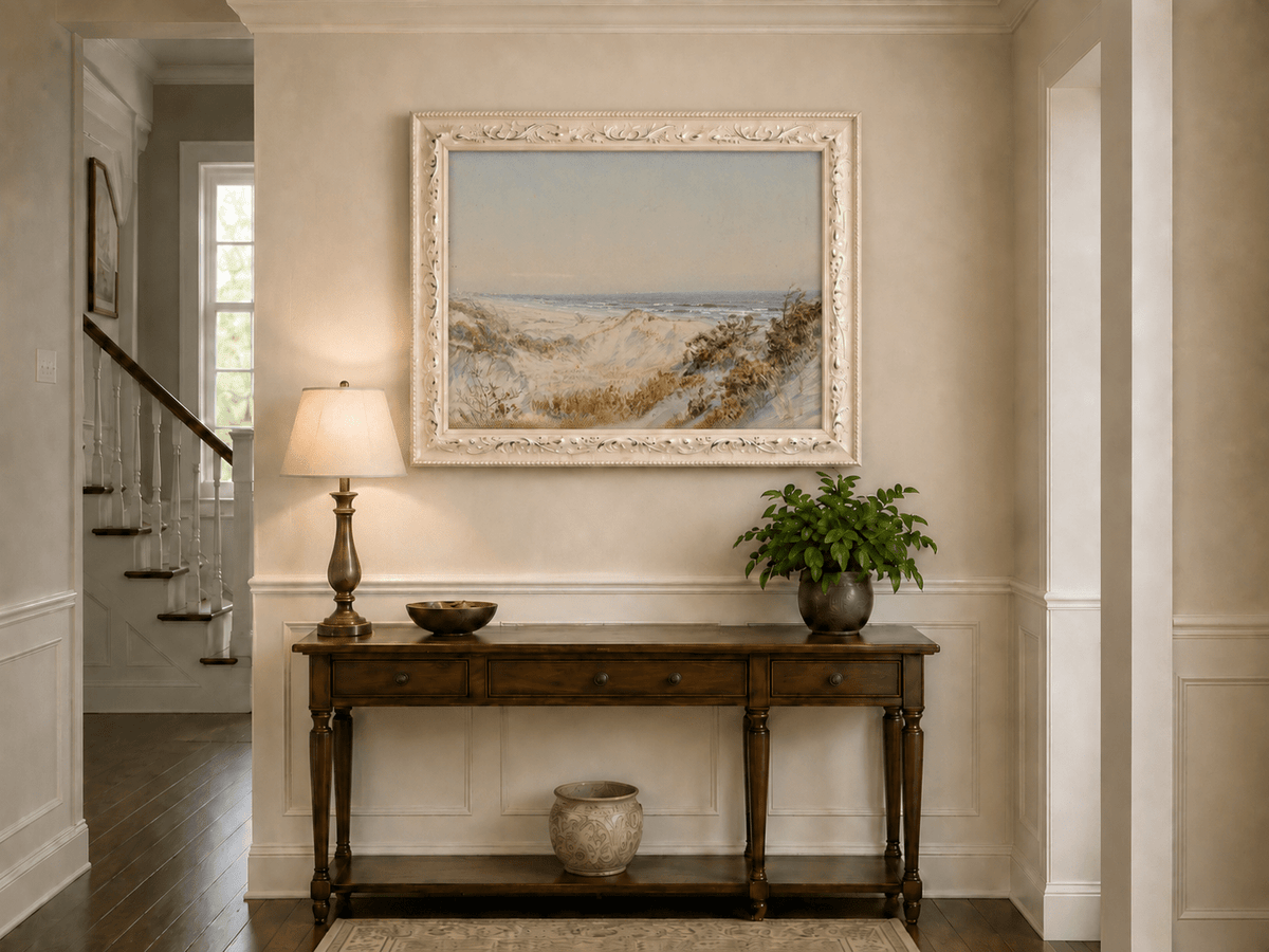 Framed hand-painted coastal oil painting with sand dunes, beach grass and a calm ocean displayed above an entryway console table.