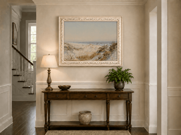 Framed hand-painted coastal oil painting with sand dunes, beach grass and a calm ocean displayed above an entryway console table.