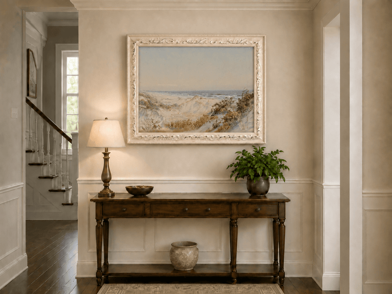 Framed hand-painted coastal oil painting with sand dunes, beach grass and a calm ocean displayed above an entryway console table.