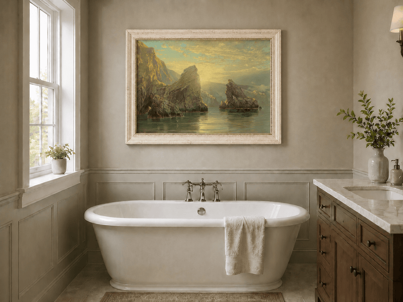 Framed hand-painted seascape oil painting with rock cliffs, calm water and glowing skies displayed above a freestanding bathtub.