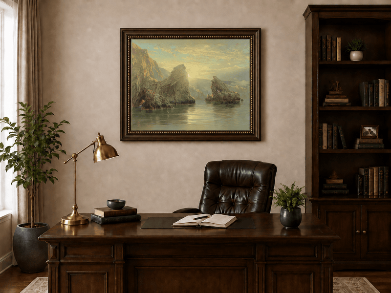 Framed hand-painted seascape oil painting with rock cliffs, calm water and glowing skies displayed above a traditional home office desk.