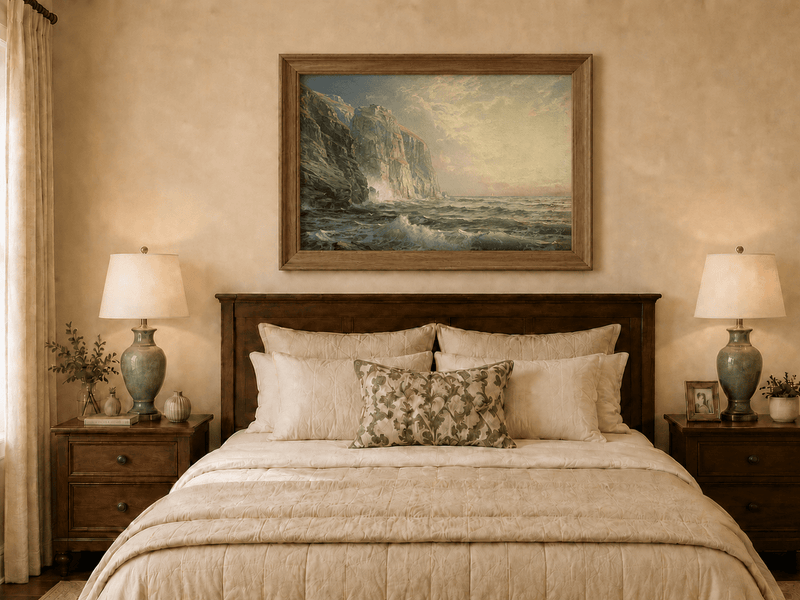 Framed hand-painted coastal oil painting with tall cliffs, rolling waves and glowing skies displayed above a wooden bed in a neutral bedroom.