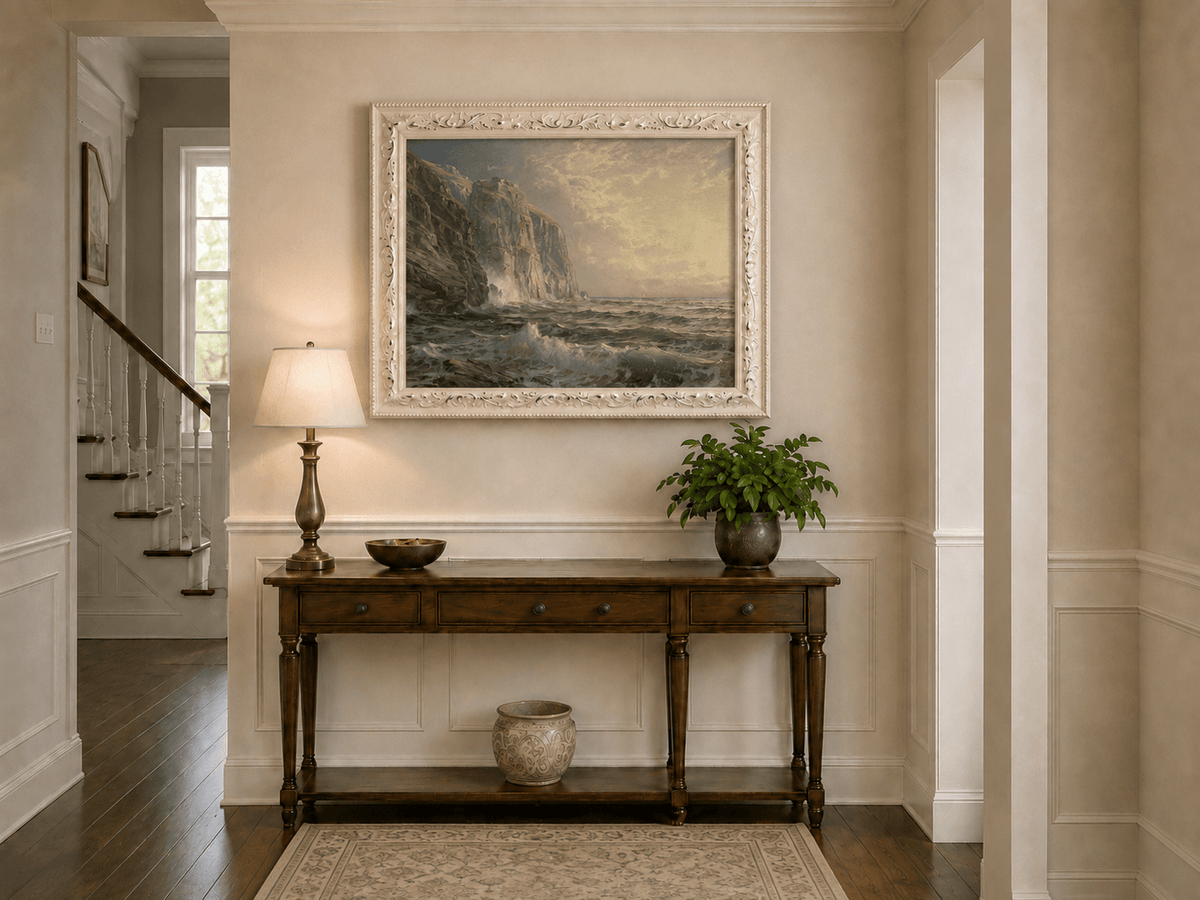 Framed hand-painted coastal oil painting with tall cliffs, rolling waves and glowing skies displayed above an entryway console table.