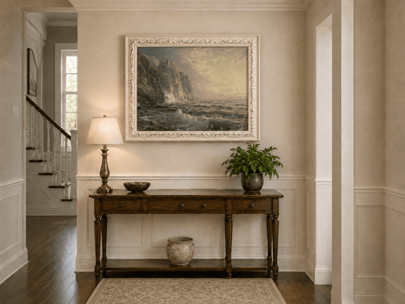 Framed hand-painted coastal oil painting with tall cliffs, rolling waves and glowing skies displayed above an entryway console table.