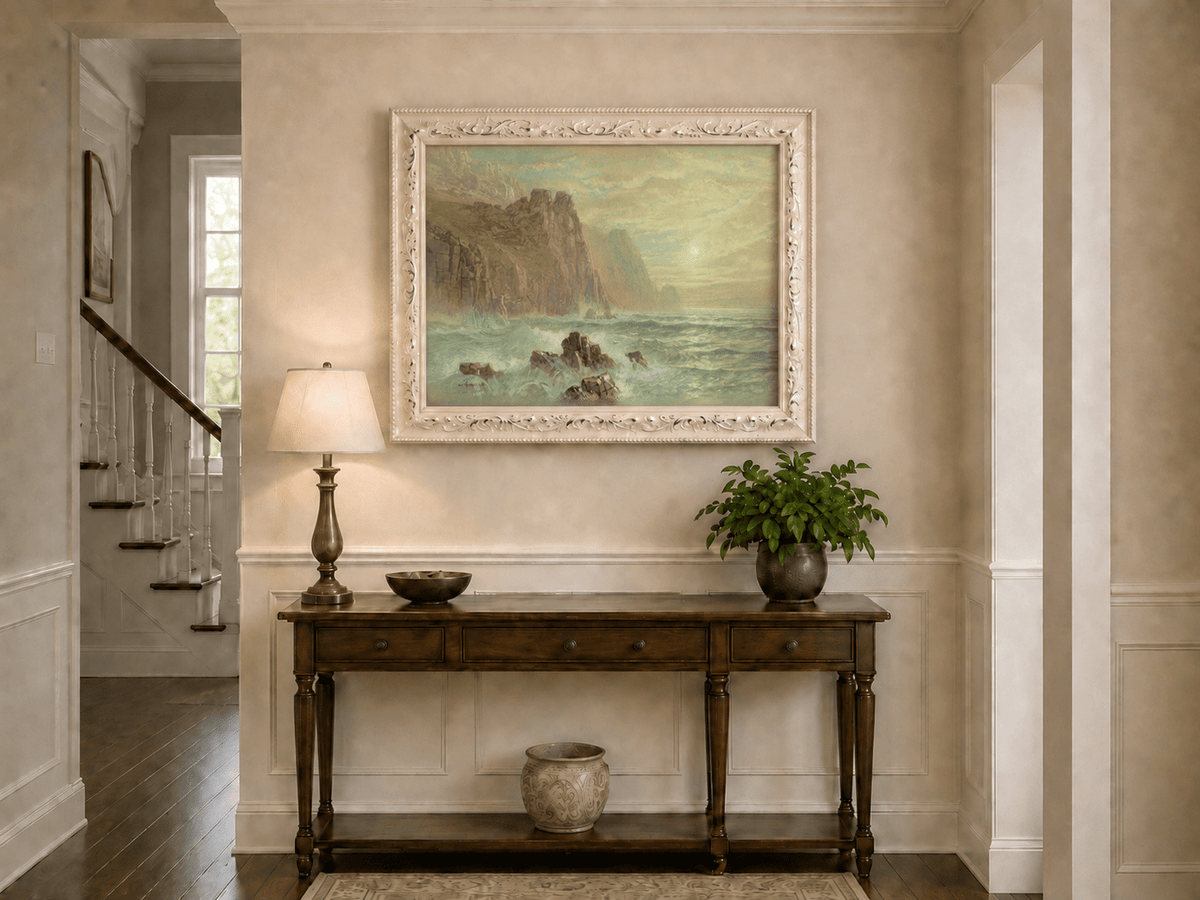 Framed hand-painted seascape oil painting with wave-washed rocks beneath soft-hued skies displayed above an entryway console table.