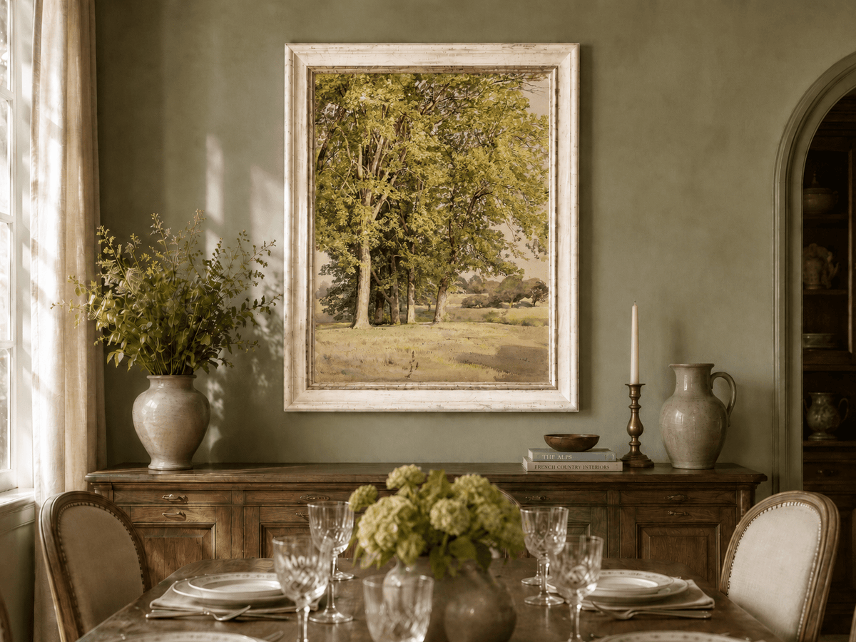 Framed hand-painted rural landscape oil painting with leafy trees and a grassy field displayed above a formal dining table.