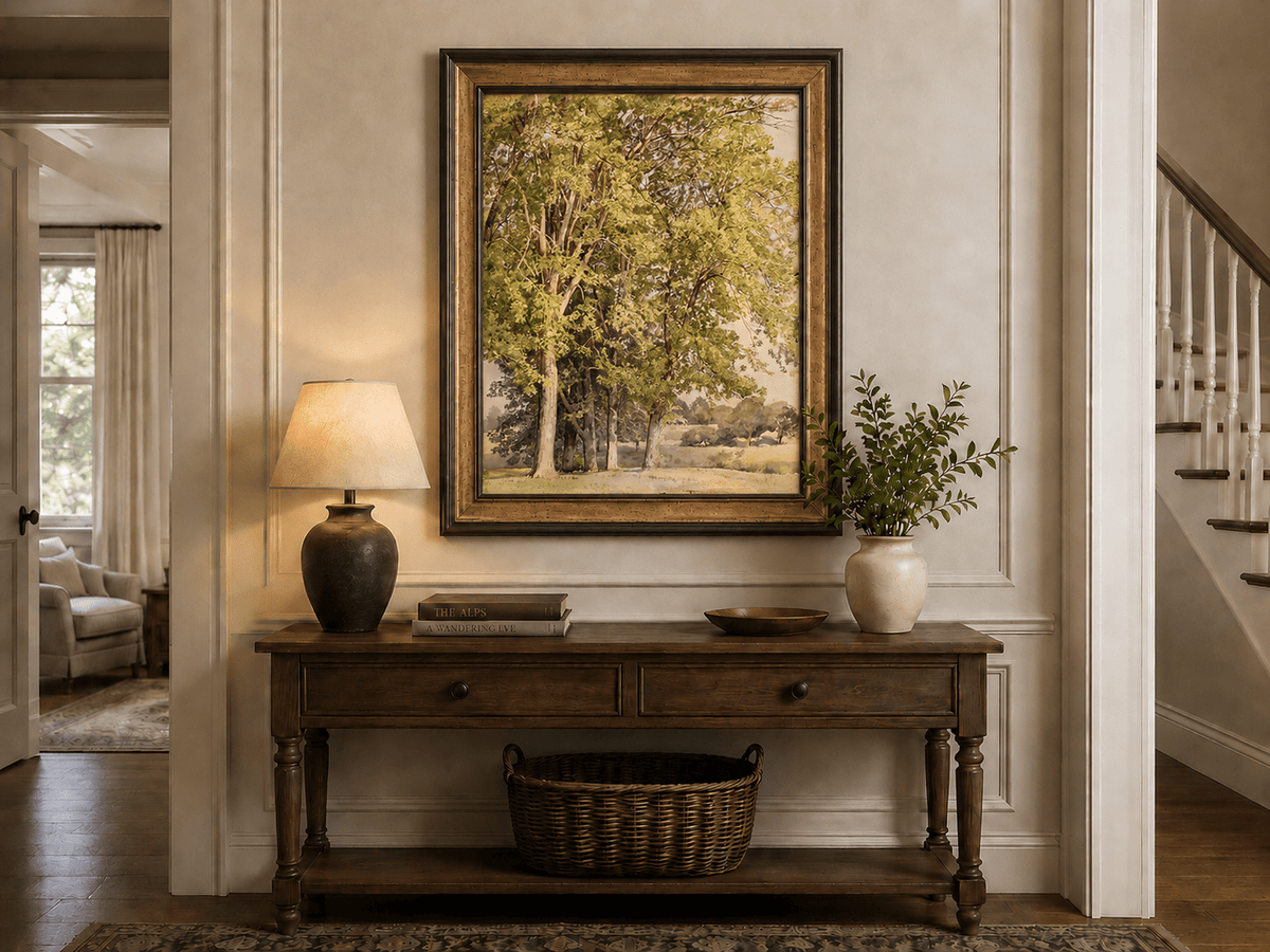 Framed hand-painted rural landscape oil painting with leafy trees and a grassy field displayed above an entryway console table.