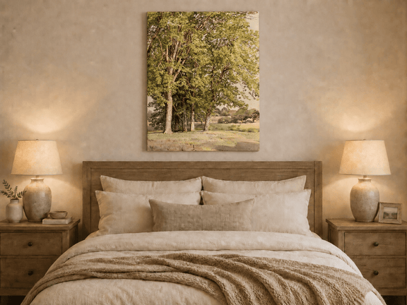 Unframed hand-painted rural landscape oil painting with leafy trees and a grassy field displayed above a wooden bed in a neutral bedroom.