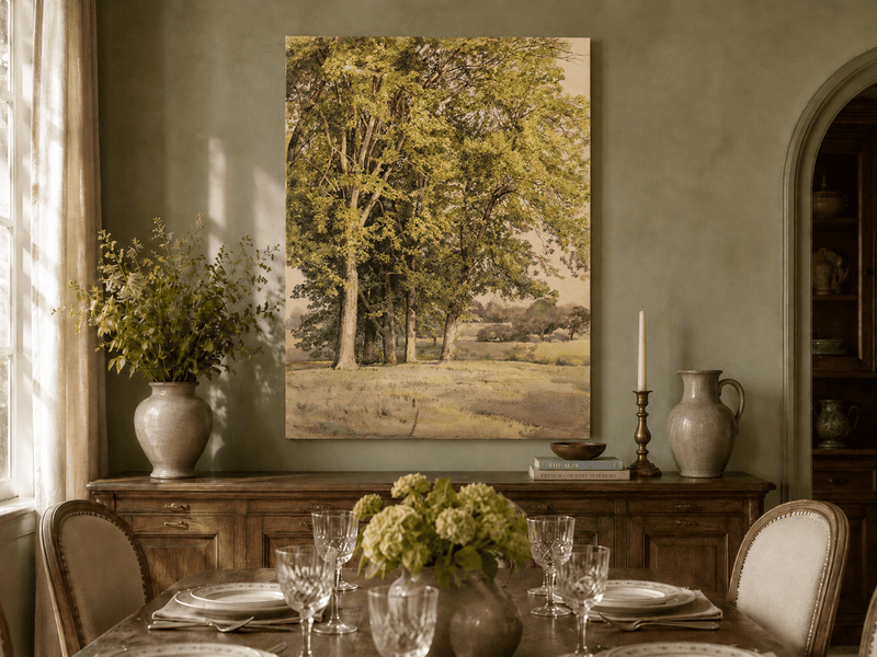 Unframed hand-painted rural landscape oil painting with leafy trees and a grassy field displayed above a formal dining table.