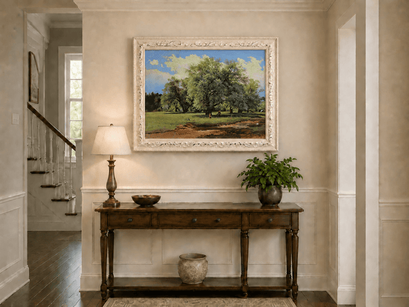 Framed hand-painted meadow oil painting with trees and small figures displayed above an entryway console table.