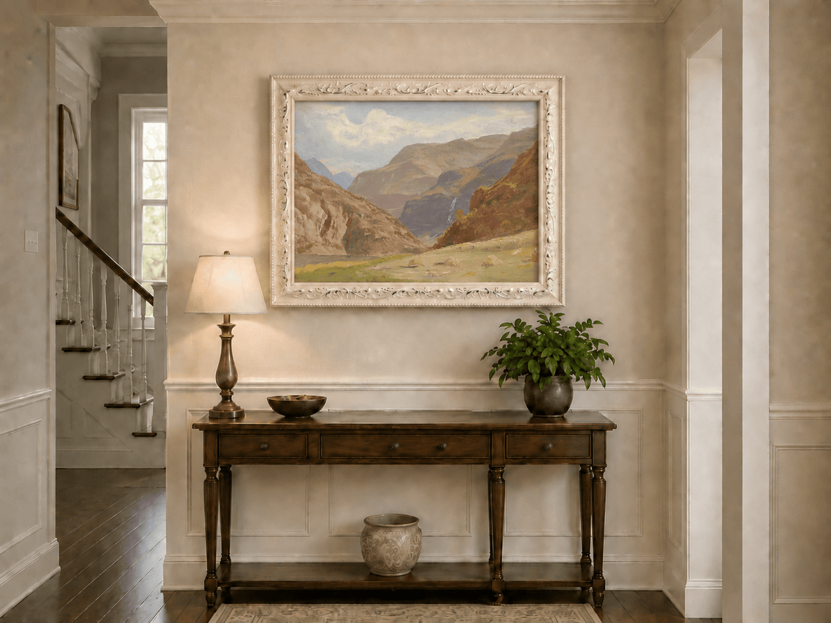 Framed hand-painted mountain canyon oil painting with a waterfall and grassy valley floor displayed above an entryway console table.