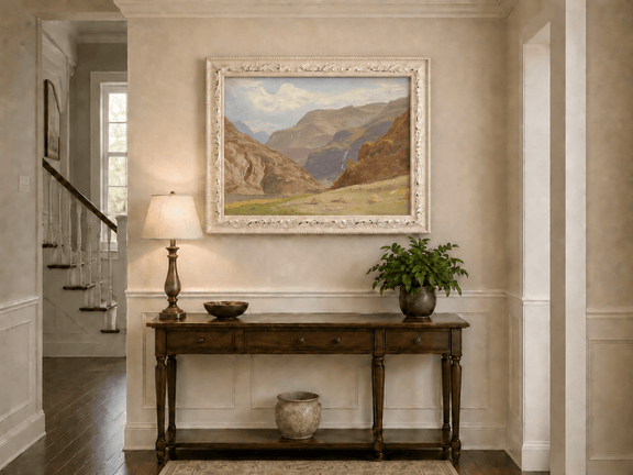 Framed hand-painted mountain canyon oil painting with a waterfall and grassy valley floor displayed above an entryway console table.