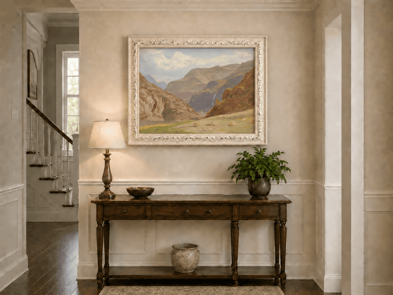 Framed hand-painted mountain canyon oil painting with a waterfall and grassy valley floor displayed above an entryway console table.