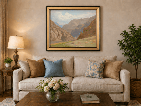 Framed hand-painted mountain canyon oil painting with a waterfall and grassy valley floor displayed above a neutral living room sofa.