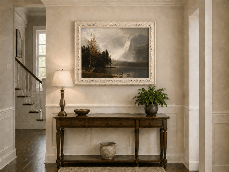 Framed hand-painted mountain lake oil painting with a deer herd and autumn trees displayed above an entryway console table.