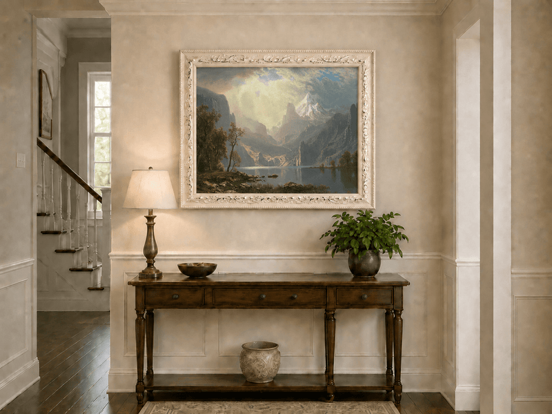 Framed hand-painted mountain lake oil painting with misty peaks in soft light displayed above an entryway console table.