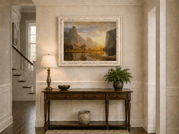 Framed hand-painted mountain lake oil painting with deer beneath a golden sunset displayed above an entryway console table.