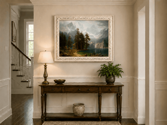 Framed hand-painted mountain lake oil painting with pine forest, waterfall and misty peaks displayed above an entryway console table.
