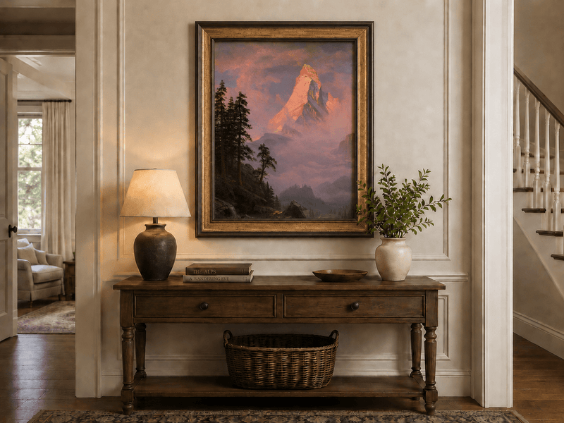 Framed hand-painted mountain oil painting with a sunlit peak, dark forest and mist displayed above an entryway console table.