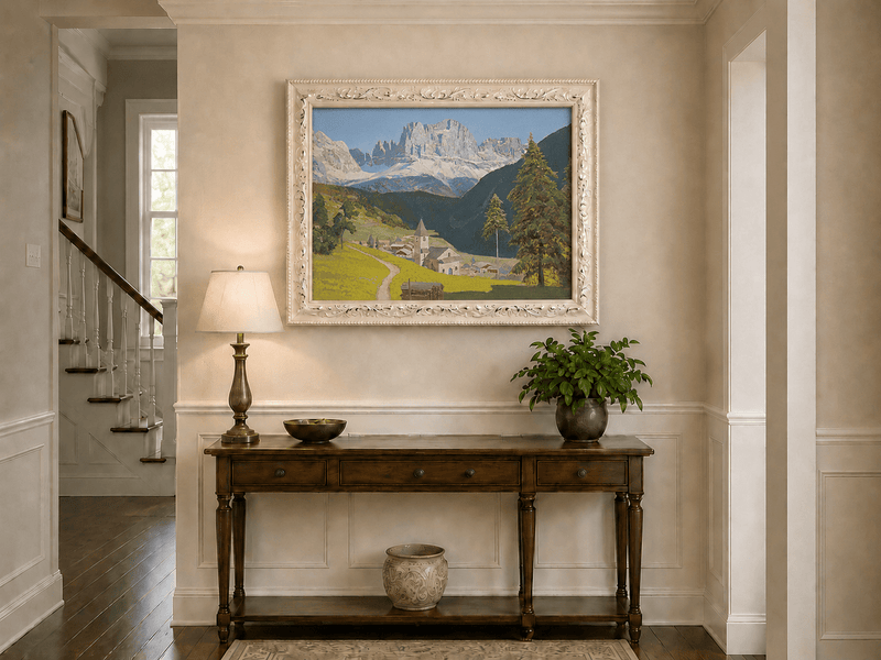 Framed hand-painted alpine landscape oil painting with a mountain village, church and path displayed above an entryway console table.