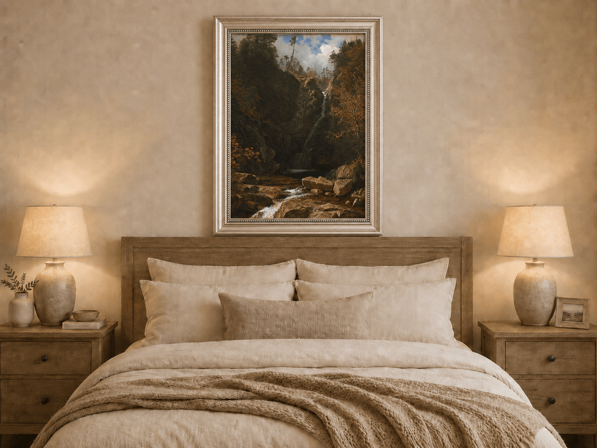 Framed hand-painted mountain waterfall oil painting through a dark autumn forest displayed above a wooden bed in a neutral bedroom.
