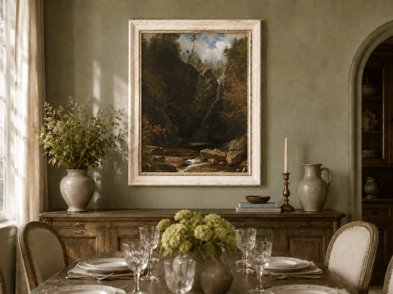 Framed hand-painted mountain waterfall oil painting through a dark autumn forest displayed above a formal dining table.