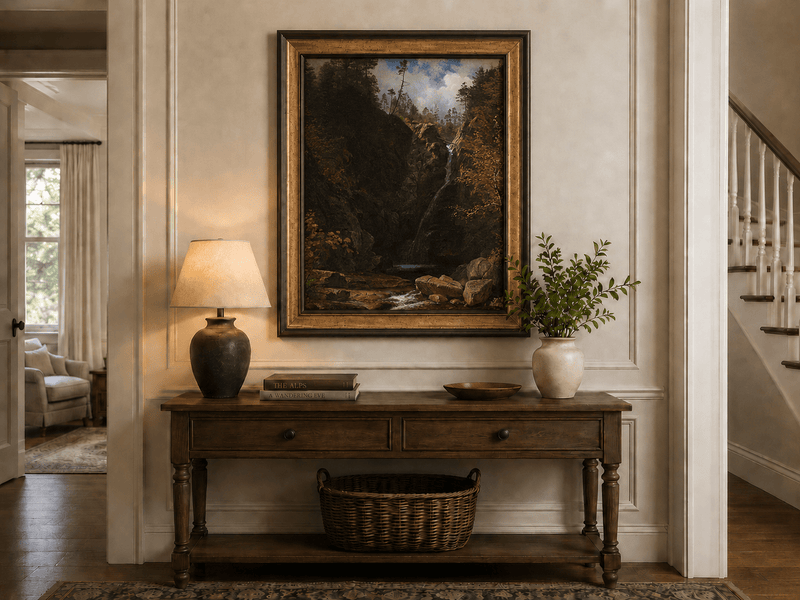 Framed hand-painted mountain waterfall oil painting through a dark autumn forest displayed above an entryway console table.