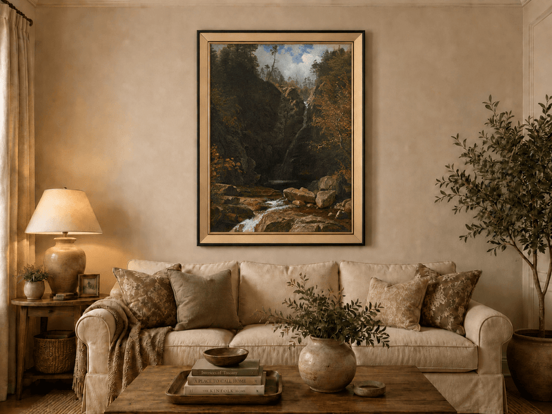 Framed hand-painted mountain waterfall oil painting through a dark autumn forest displayed above a neutral living room sofa.