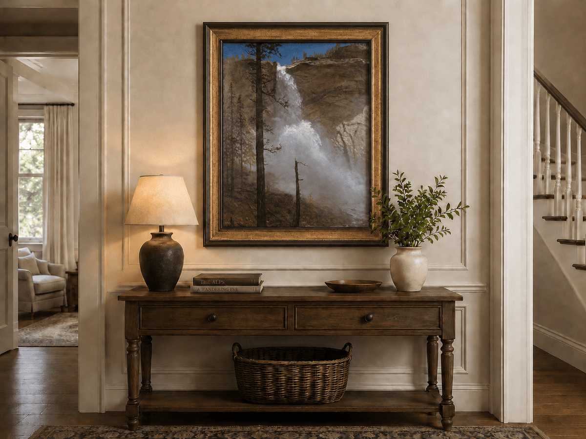 Framed hand-painted mountain waterfall oil painting with rocky cliffs and pine forest displayed above an entryway console table.