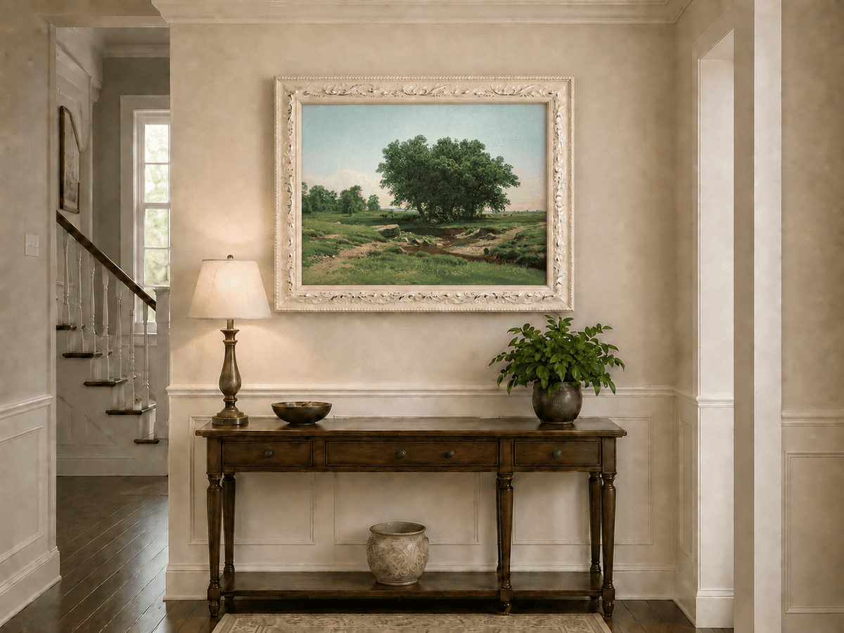 Framed hand-painted pastoral landscape oil painting with broad trees and a winding stream displayed above an entryway console table.