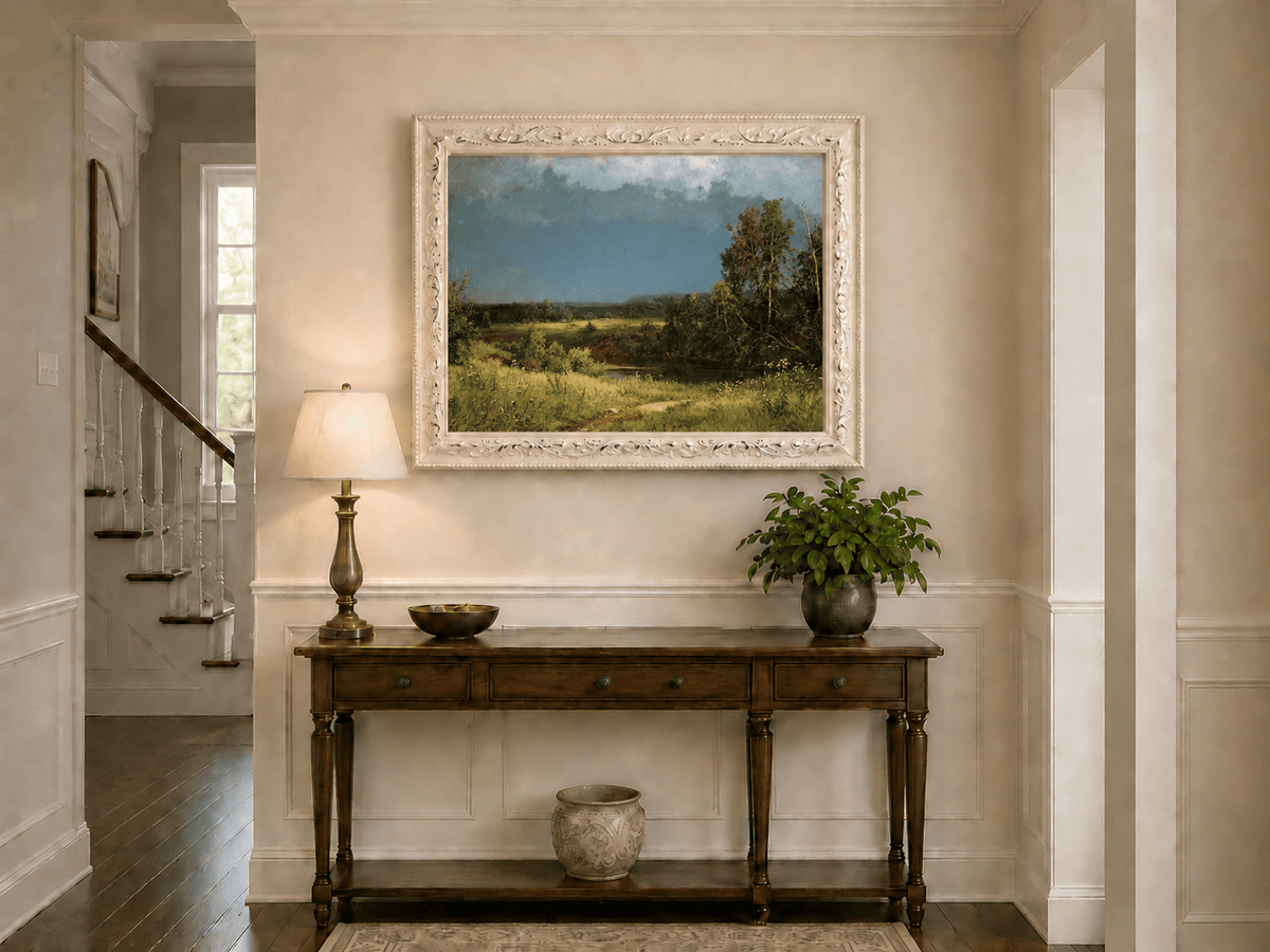 Framed hand-painted river meadow oil painting beneath a dramatic stormy sky displayed above an entryway console table.