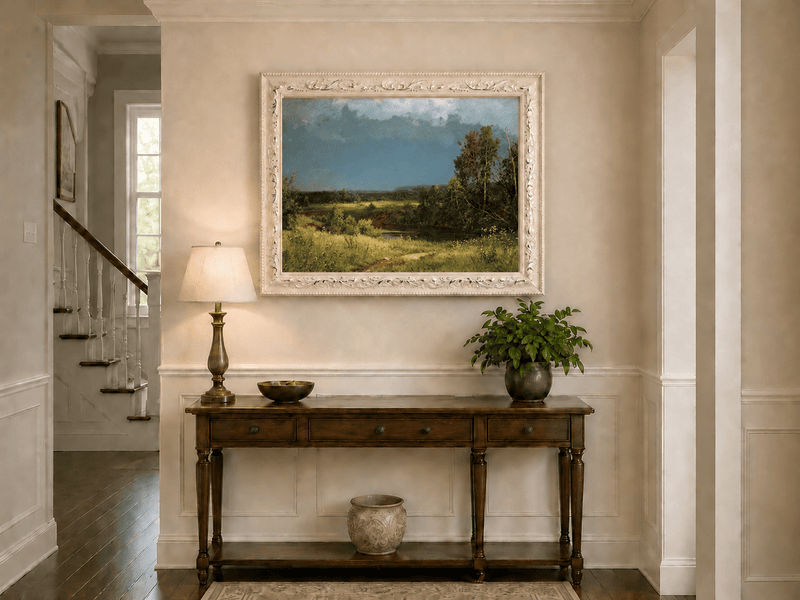 Framed hand-painted river meadow oil painting beneath a dramatic stormy sky displayed above an entryway console table.