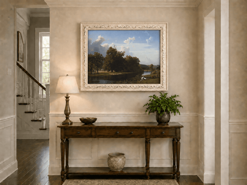 Framed hand-painted riverside oil painting with a large oak tree, boat and distant cottage displayed above an entryway console table.
