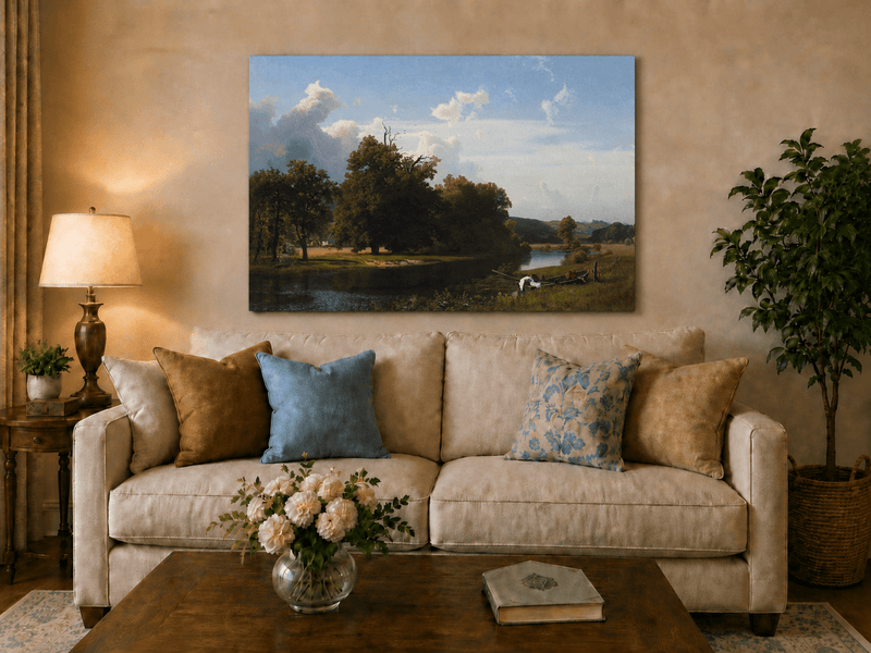 Unframed hand-painted riverside oil painting with a large oak tree, boat and distant cottage displayed above a neutral living room sofa.
