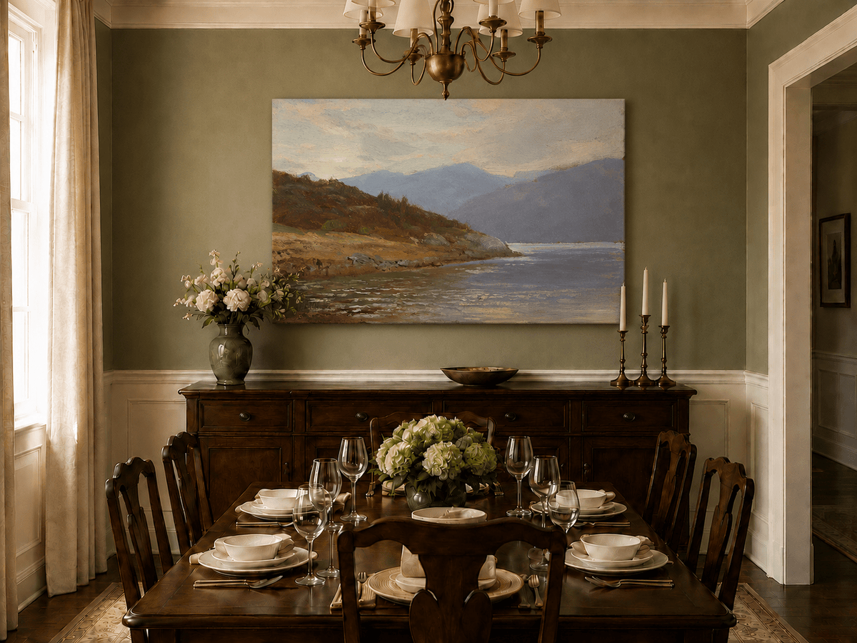 Unframed hand-painted lake shore oil painting with rocky banks, vegetation and mountain ranges displayed above a formal dining table.