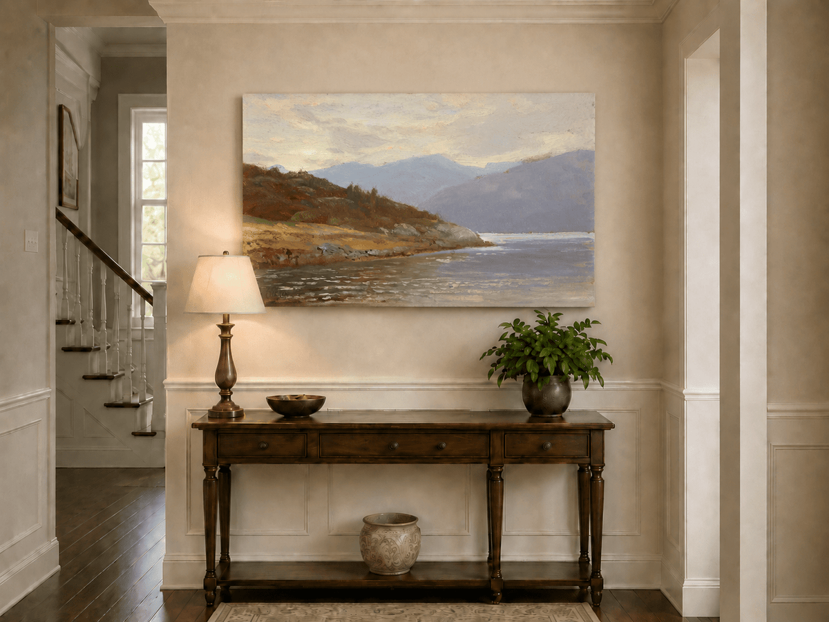 Unframed hand-painted lake shore oil painting with rocky banks, vegetation and mountain ranges displayed above an entryway console table.
