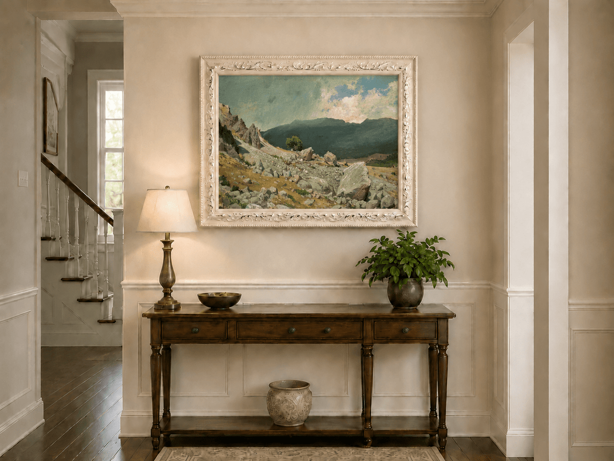 Framed hand-painted alpine oil painting with a rocky slope and distant mountain peaks displayed above an entryway console table.