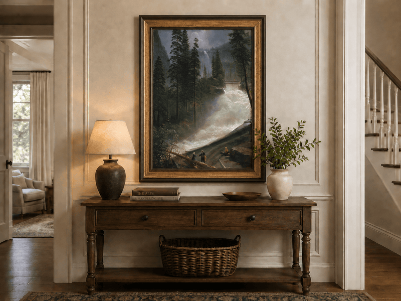 Framed hand-painted forest oil painting with figures beside a rushing river and waterfall displayed above an entryway console table.