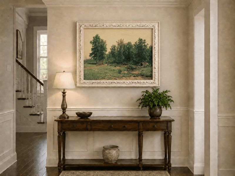 Framed hand-painted rustic meadow oil painting with a stream and distant forest edge displayed above an entryway console table.