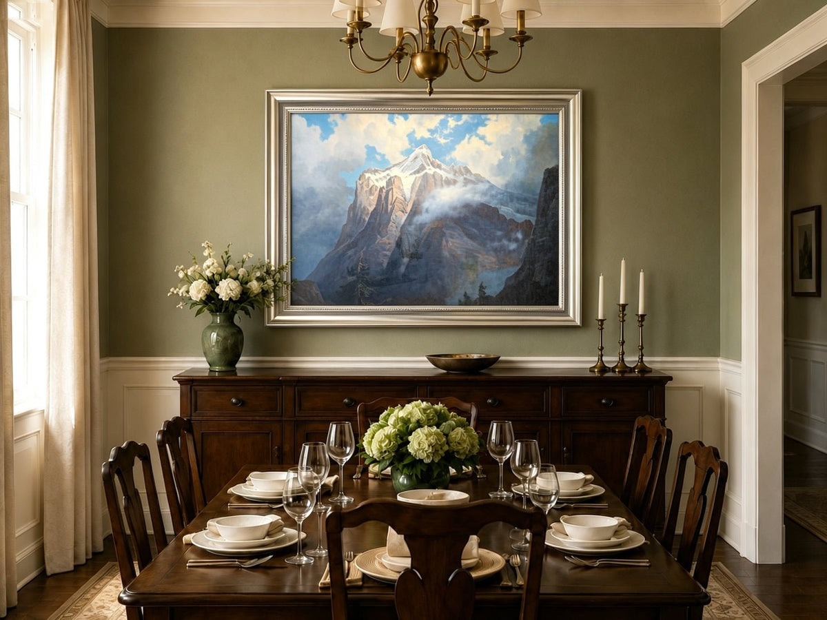 Framed hand-painted snow-capped mountain oil painting rising through luminous mist displayed above a formal dining table.