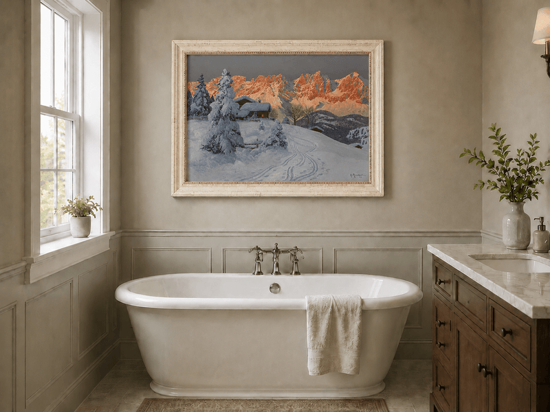 Framed hand-painted winter alpine oil painting with a snowy cabin and mountains at sunset displayed above a freestanding bathtub.