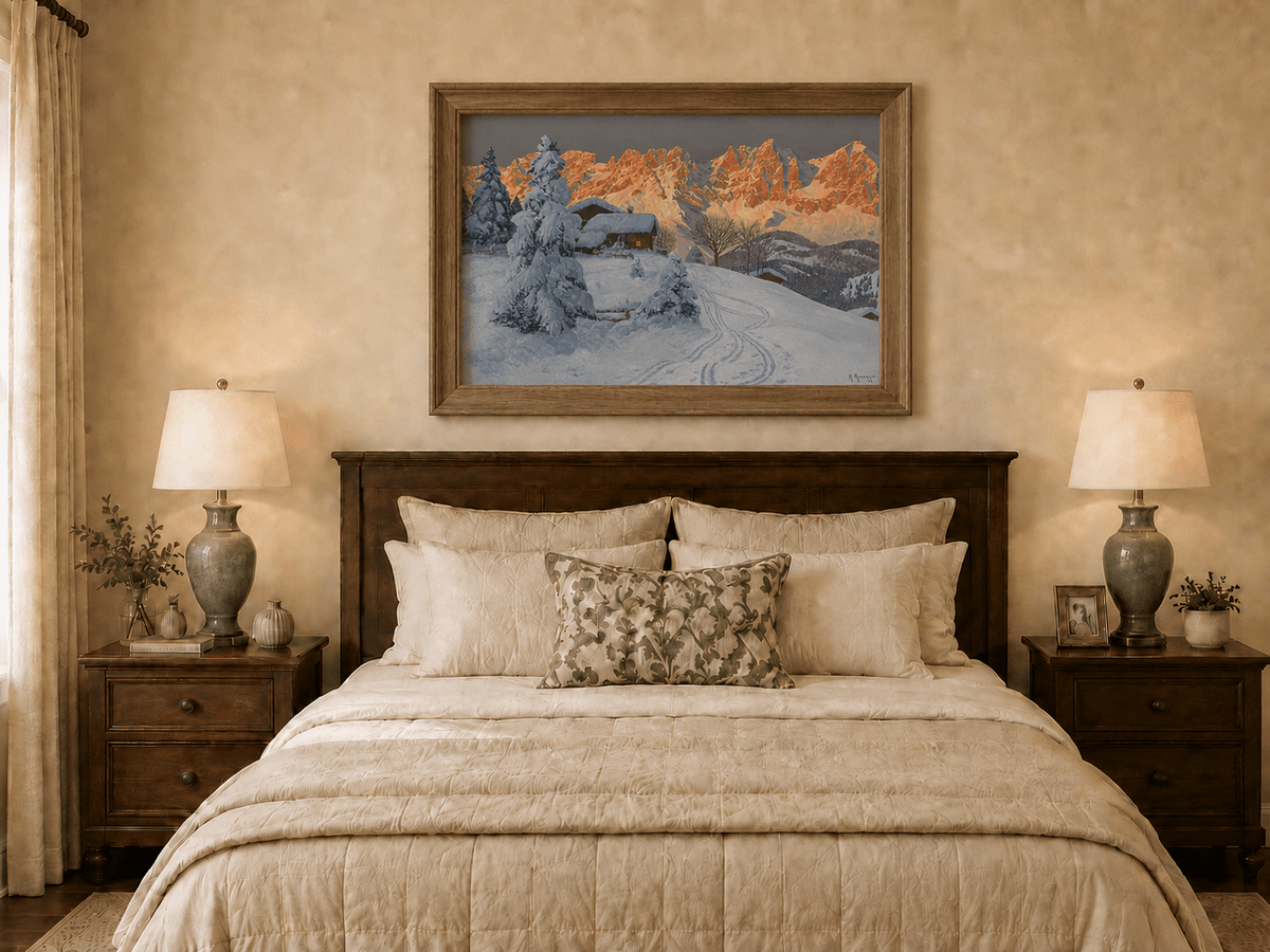 Framed hand-painted winter alpine oil painting with a snowy cabin and mountains at sunset displayed above a wooden bed in a neutral bedroom.