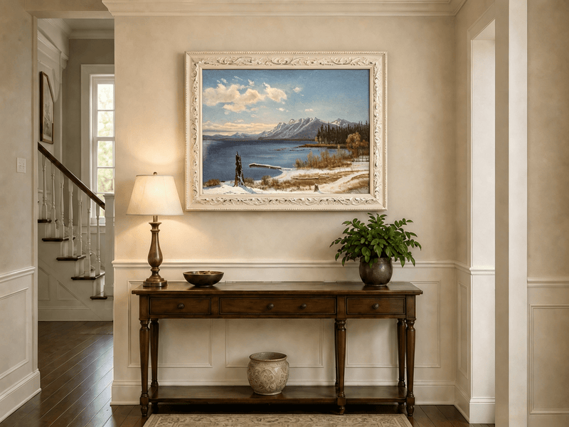 Framed hand-painted snowy lake oil painting with a winter path and distant mountain view displayed above an entryway console table.