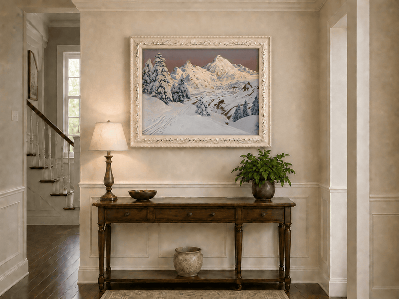 Framed hand-painted snowy mountain oil painting with pine trees and tracks through the snow displayed above an entryway console table.