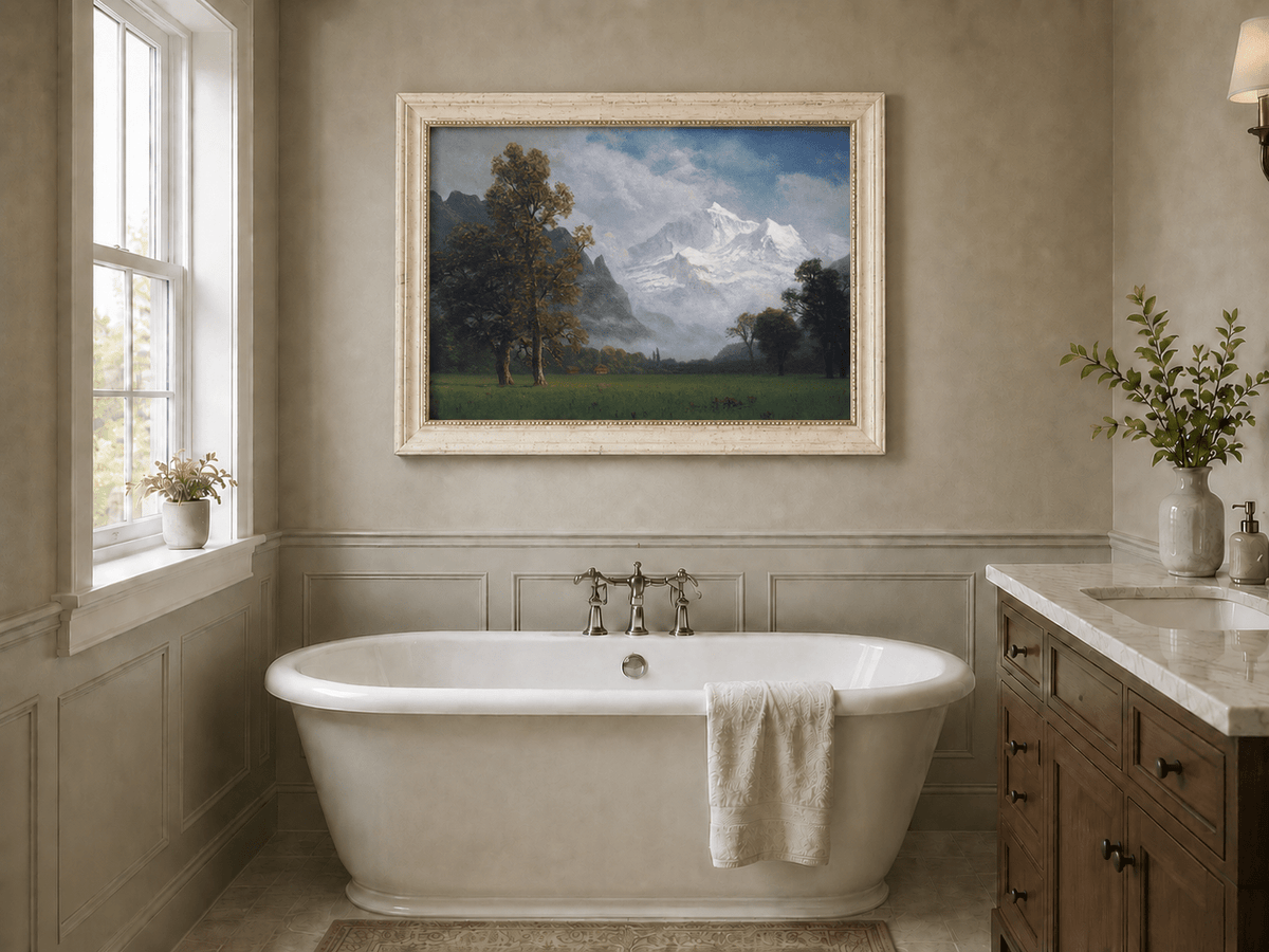 Framed hand-painted snowy mountain valley oil painting with a meadow and tall trees displayed above a freestanding bathtub.
