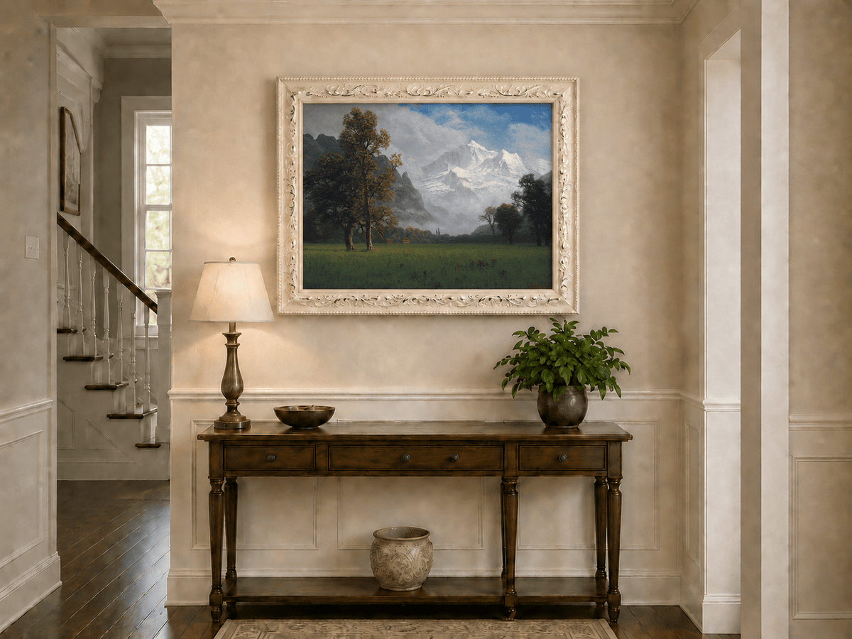 Framed hand-painted snowy mountain valley oil painting with a meadow and tall trees displayed above an entryway console table.